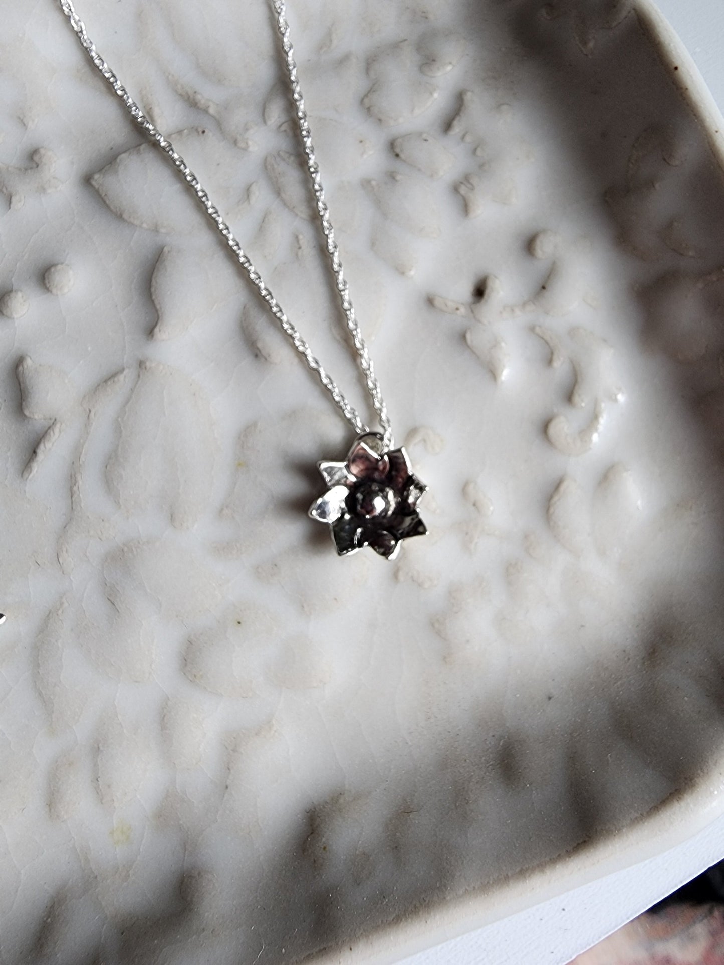 Tiny flower pendant hanging from a dainty silver chain