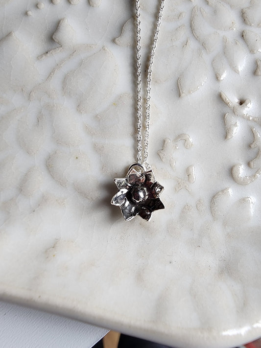 Tiny flower pendant hanging from a dainty silver chain