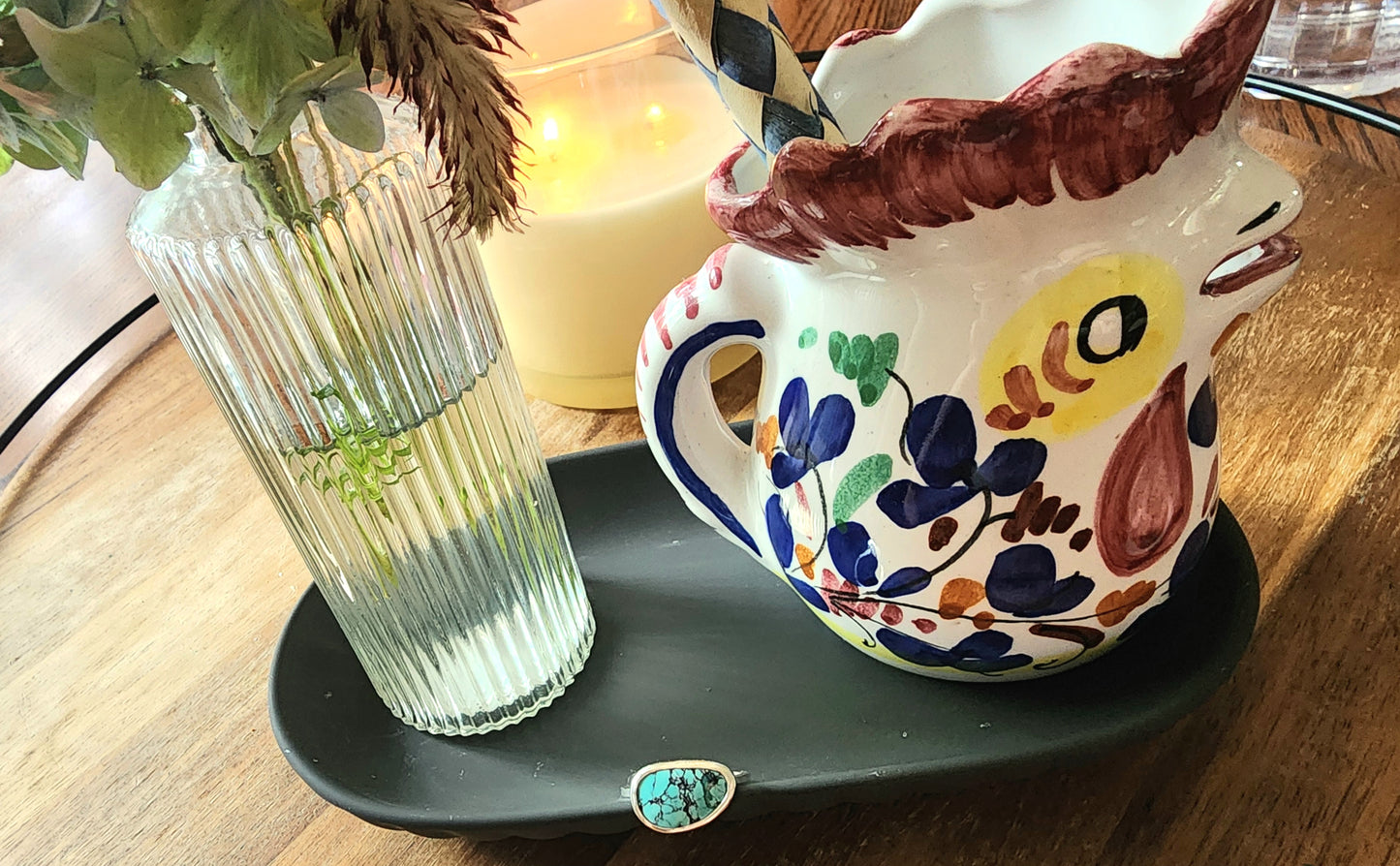 Decorative ceramic owl mug with floral patterns on a dark plate, next to a clear vase with greenery.