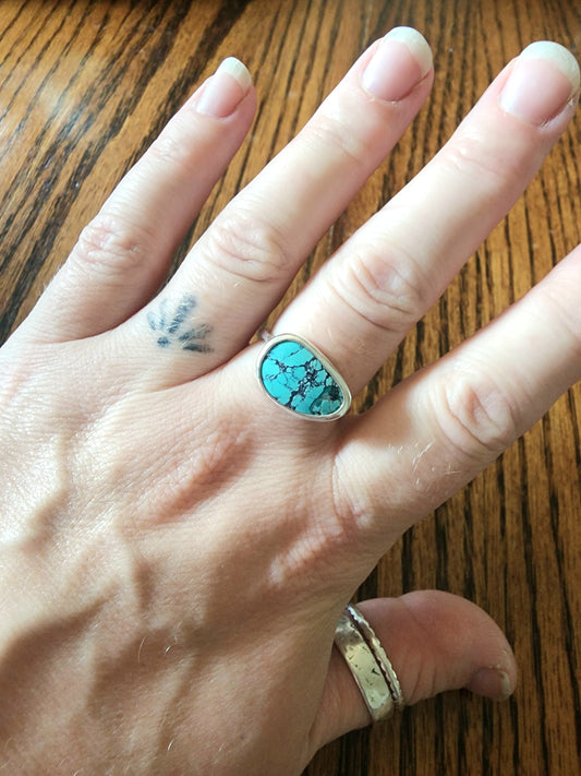 Hand wearing a turquoise ring on a wooden surface
