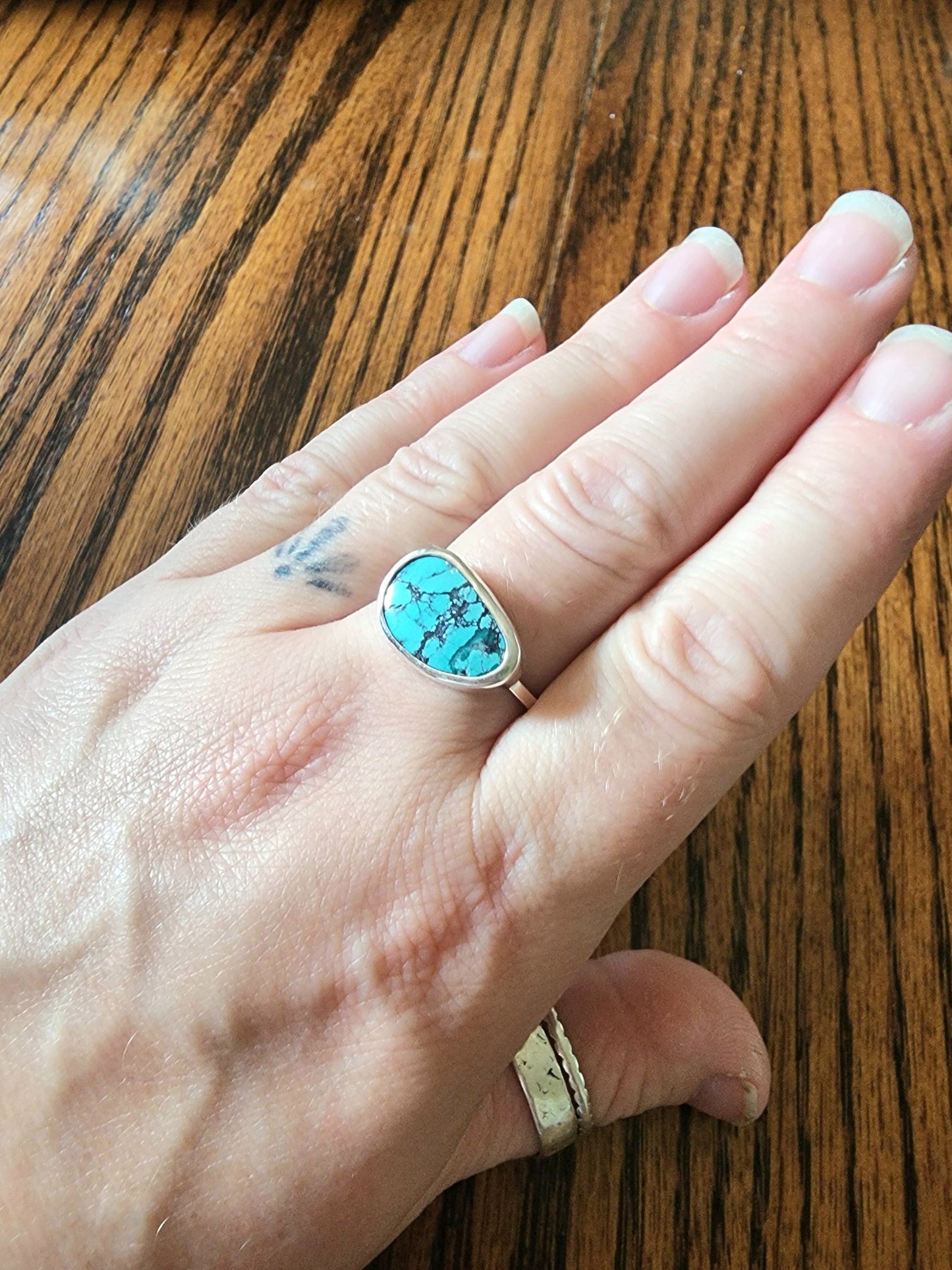 Hand wearing a turquoise ring on a wooden surface