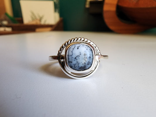 square stone that is white with black small dots surrounded by a circle, top circle is twist silver, bottom part of circle is smooth circle