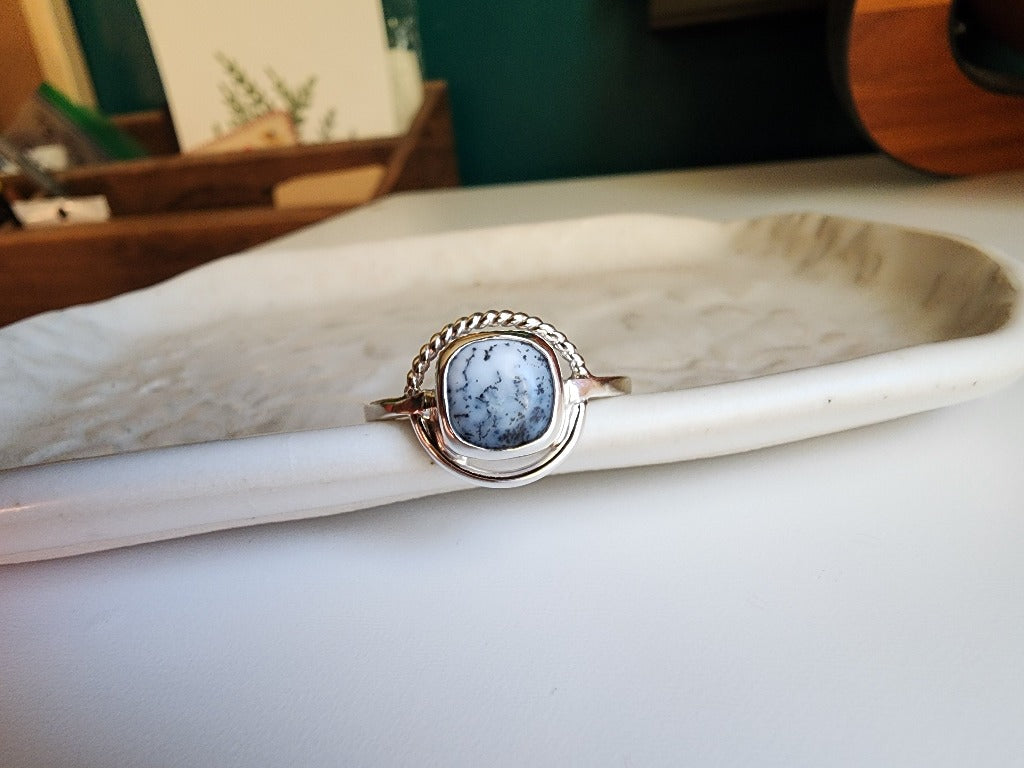 square stone that is white with black small dots surrounded by a circle, top circle is twist silver, bottom part of circle is smooth circle