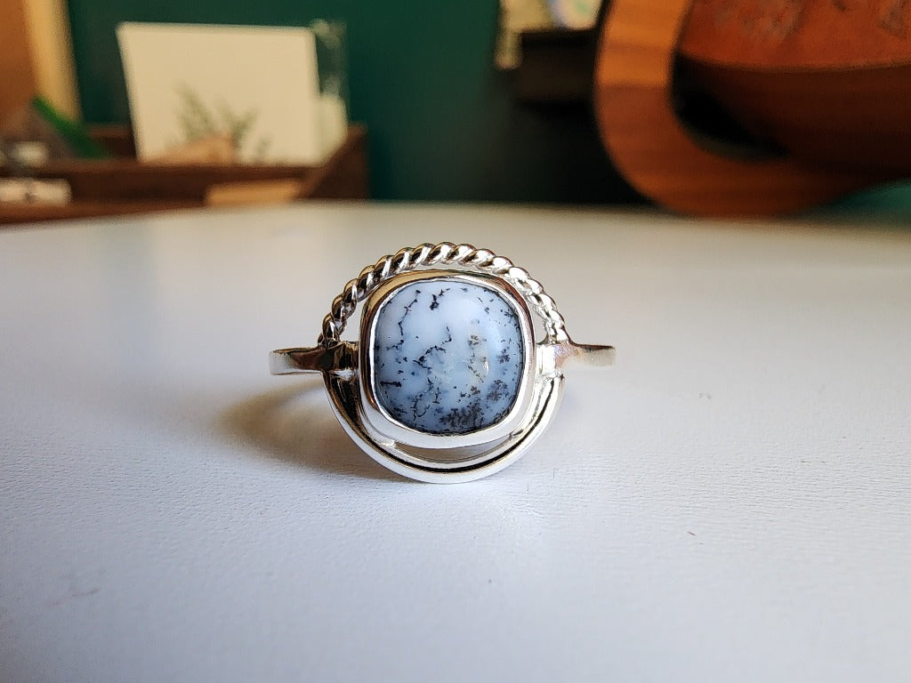 square stone that is white with black small dots surrounded by a circle, top circle is twist silver, bottom part of circle is smooth circle