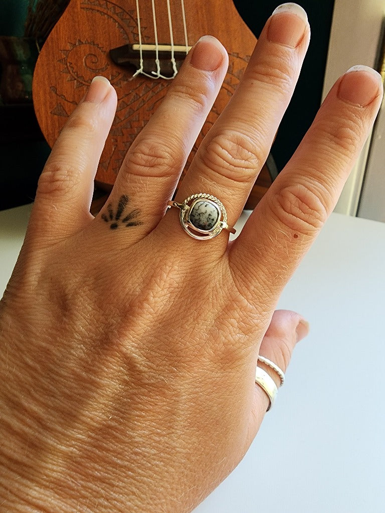 square stone that is white with black small dots surrounded by a circle, top circle is twist silver, bottom part of circle is smooth circle