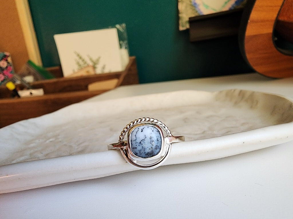 square stone that is white with black small dots surrounded by a circle, top circle is twist silver, bottom part of circle is smooth circle