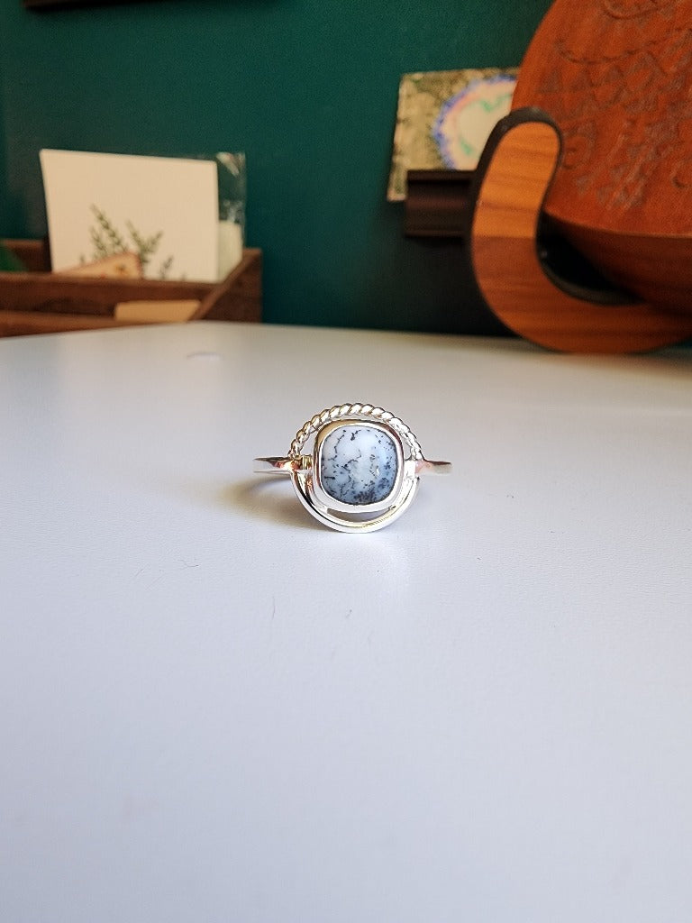 square stone that is white with black small dots surrounded by a circle, top circle is twist silver, bottom part of circle is smooth circle