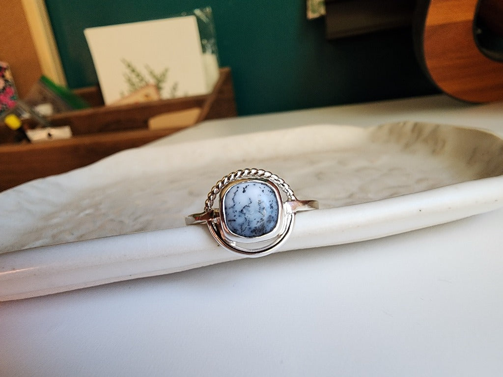square stone that is white with black small dots surrounded by a circle, top circle is twist silver, bottom part of circle is smooth circle