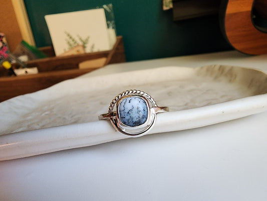 square stone that is white with black small dots surrounded by a circle, top circle is twist silver, bottom part of circle is smooth circle