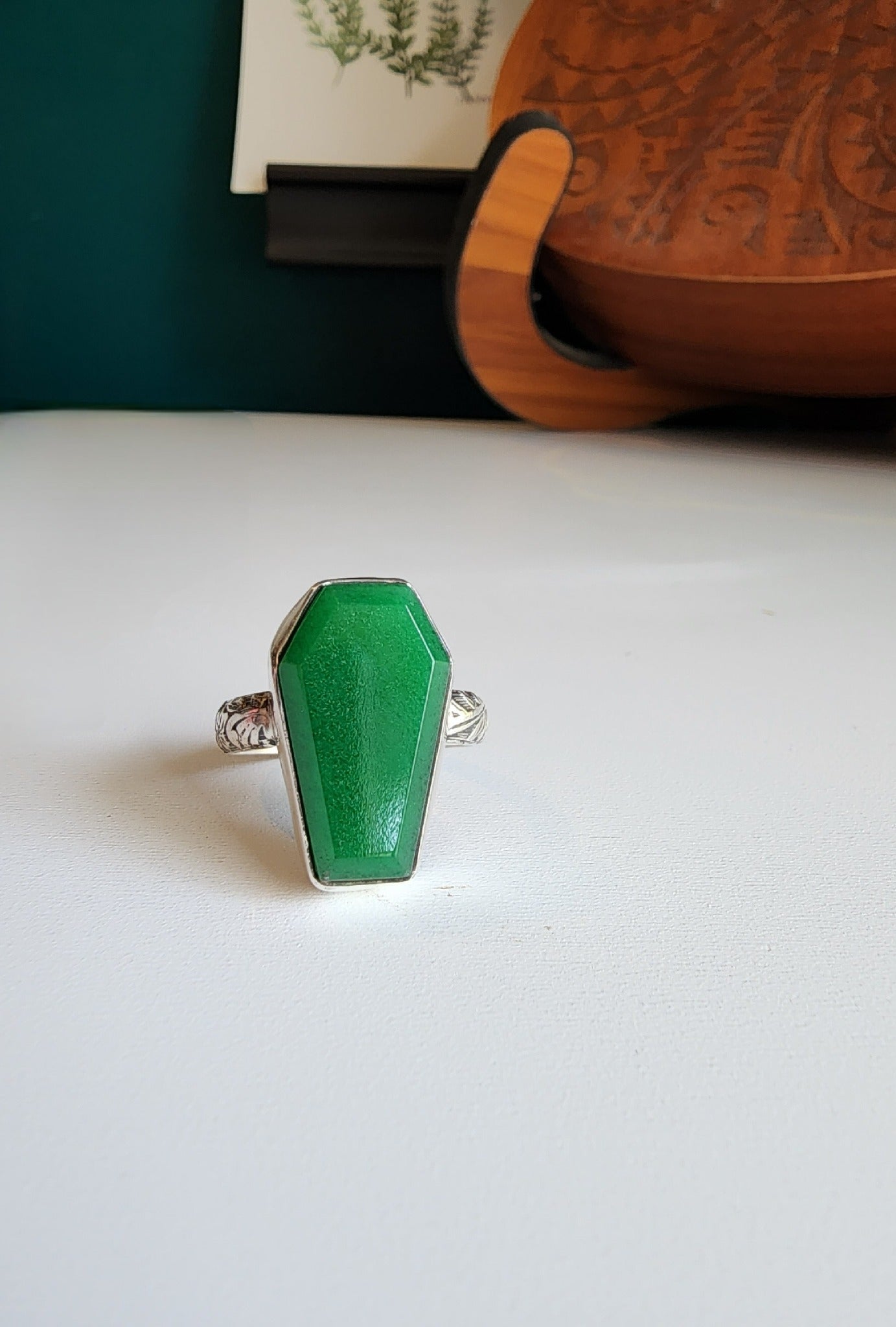 Jade coffin stone shaped stone with simple bezel surround, single band with flowers and vine details that stand out.