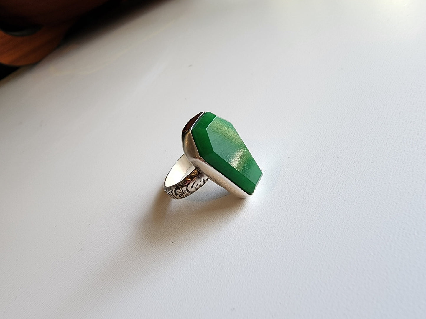 Jade coffin stone shaped stone with simple bezel surround, single band with flowers and vine details that stand out.