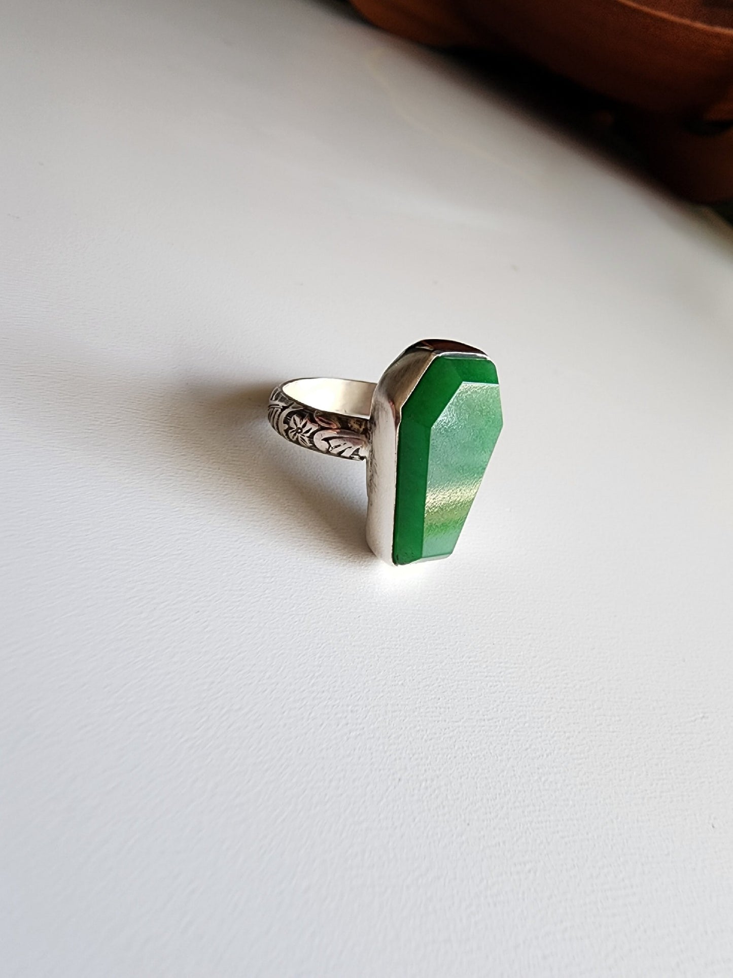 Jade coffin stone shaped stone with simple bezel surround, single band with flowers and vine details that stand out.