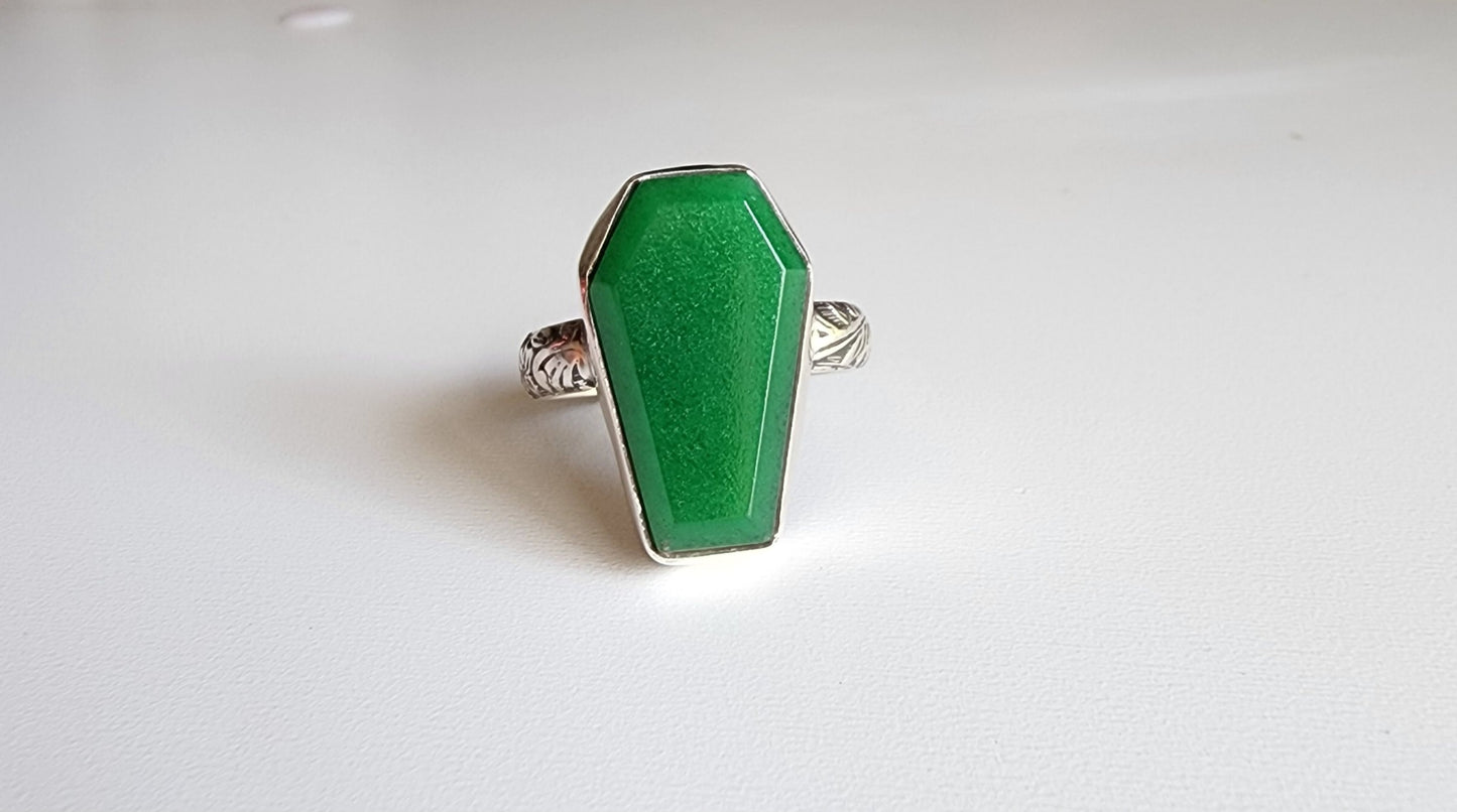 Jade coffin stone shaped stone with simple bezel surround, single band with flowers and vine details that stand out.