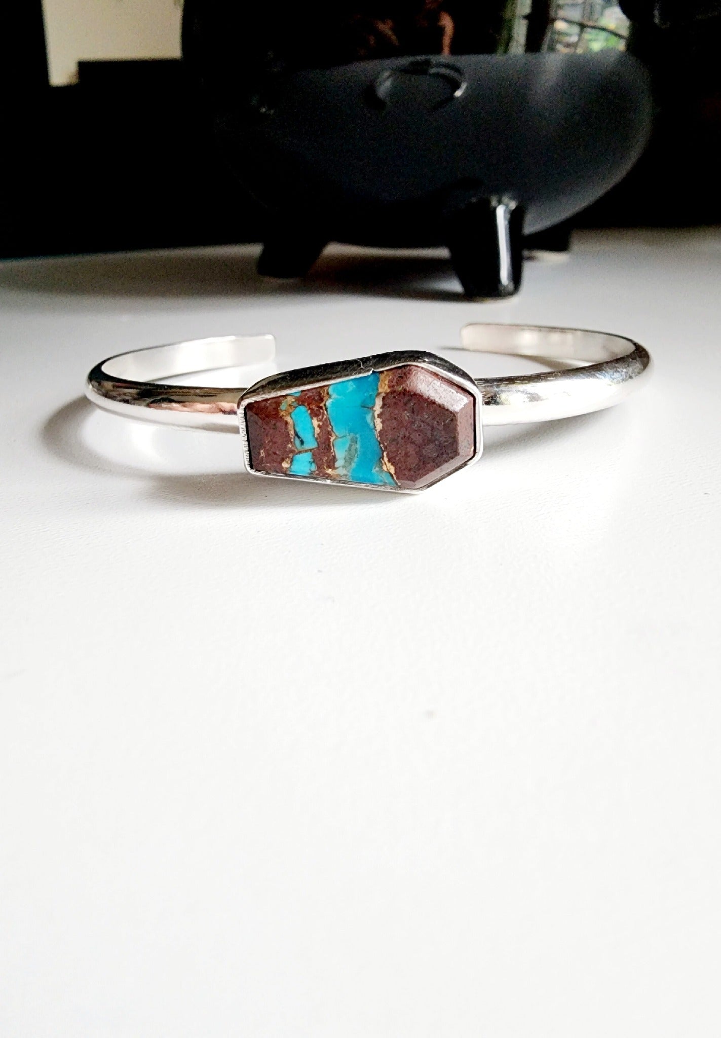 a coffin shaped stone that is blue and red (lave copper turquoise) mounted on a simple sterling silver cuff