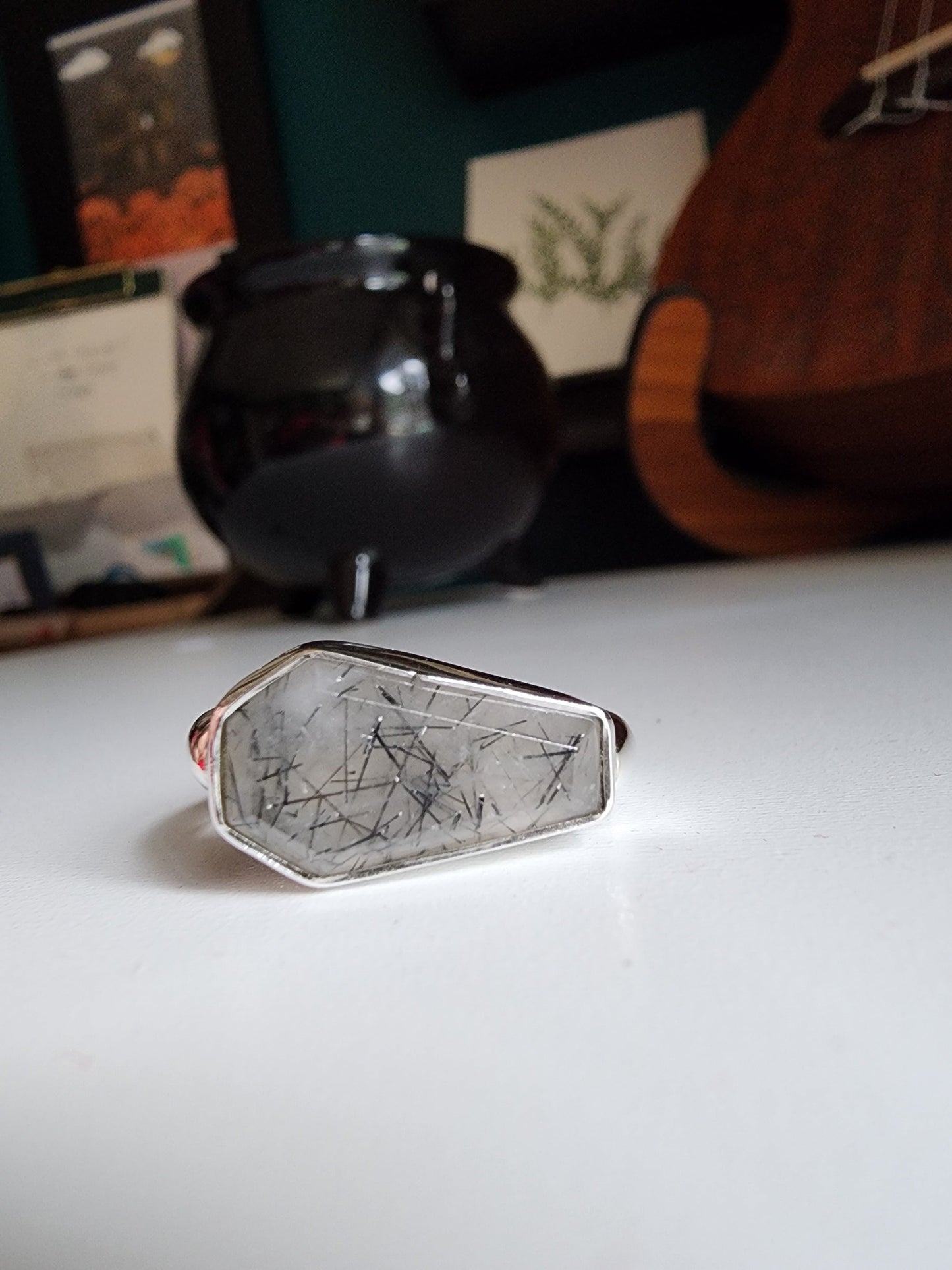 white stone with black flecks with metallic coffin stone shaped ring with thick band that meets the bezel on the left and right