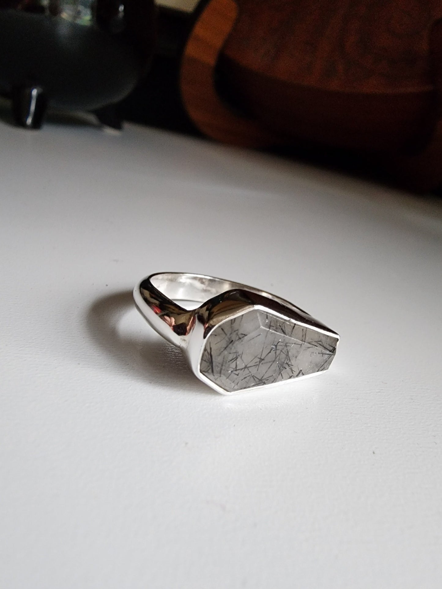 white stone with black flecks with metallic coffin stone shaped ring with thick band that meets the bezel on the left and right