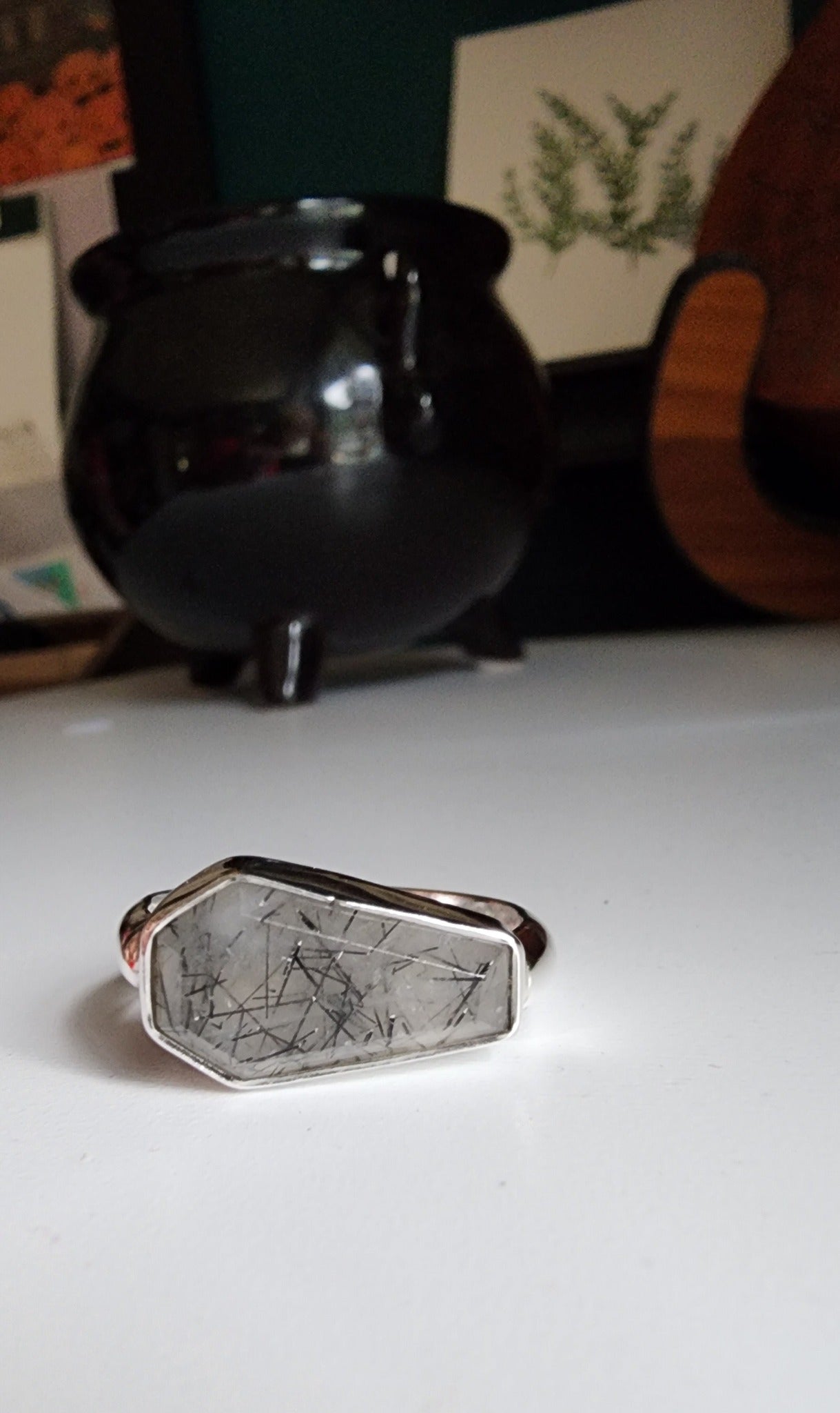 white stone with black flecks with metallic coffin stone shaped ring with thick band that meets the bezel on the left and right
