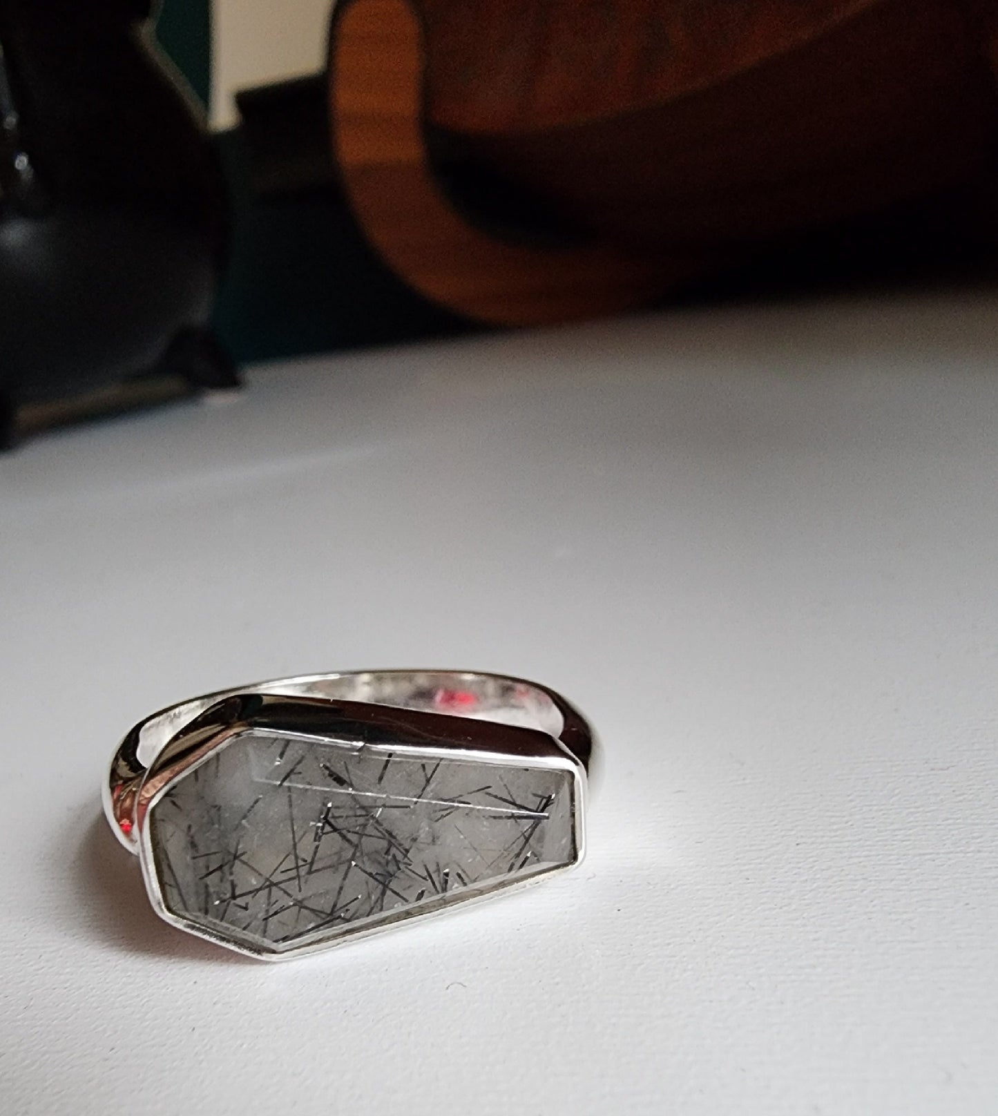 white stone with black flecks with metallic coffin stone shaped ring with thick band that meets the bezel on the left and right