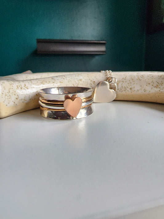 Silver textured wide band ring with three bands top band gold, middle band silver with a rose gold heart, bottom band is gold. Three bands mounted on a wide ring that spin freely, perfect for spinning of rings