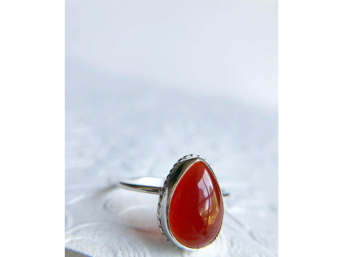 Pear shaped red ring with open back bezel, bezel mounts to the left and right side of the stone.