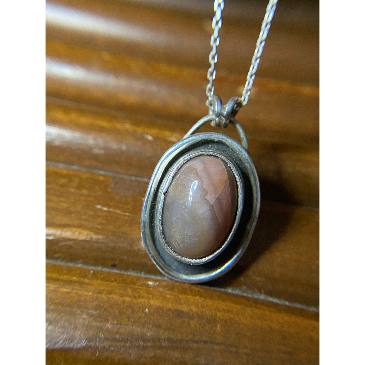 Oval pink stone with silver surround encircling stone, mounted on a 18 ich sterling silver necklace this is a choker style chain.
