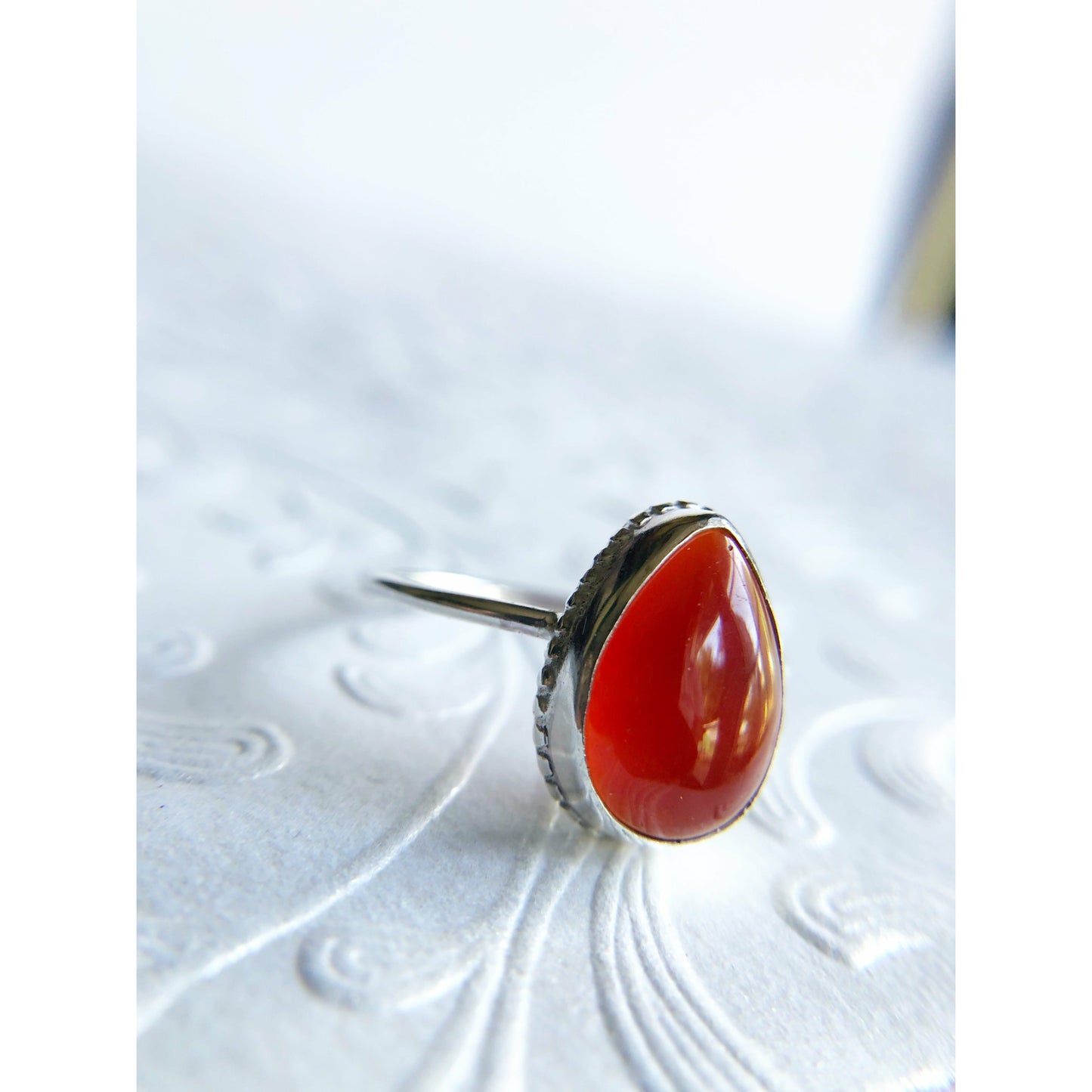 Pear shaped red ring with open back bezel, bezel mounts to the left and right side of the stone.