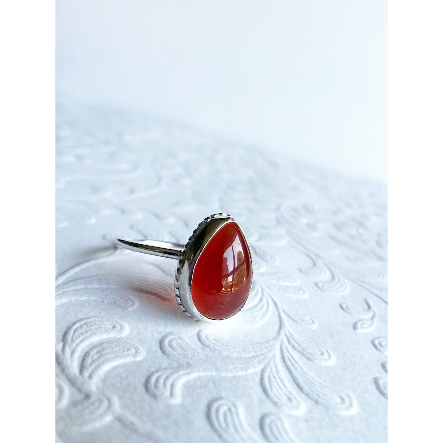 Pear shaped red ring with open back bezel, bezel mounts to the left and right side of the stone.