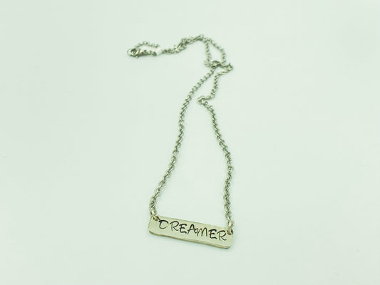 Bar of silver in a square with rounded corners, dreamer is hand stamped and darkened with black patina to pop against the silver.