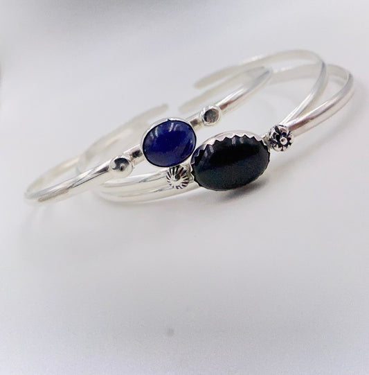 Stacakble cuffs with onyx, lapis or just a plain bracelet. Ornate pieces of silver dot the pieces as well as a oval stone.