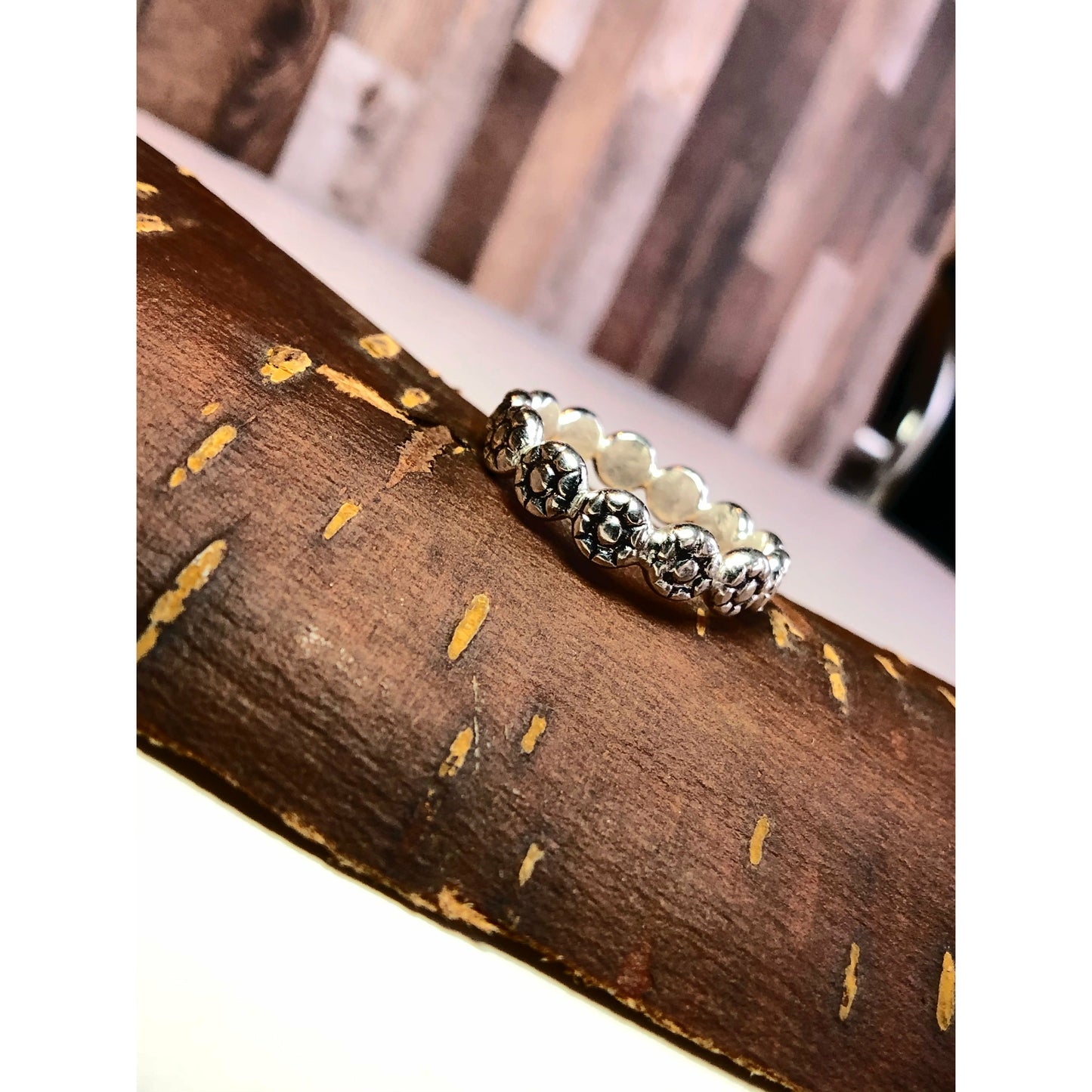 Flat square shaped ring with flowers imprinted on ring face. Repeat pattern all the way around.