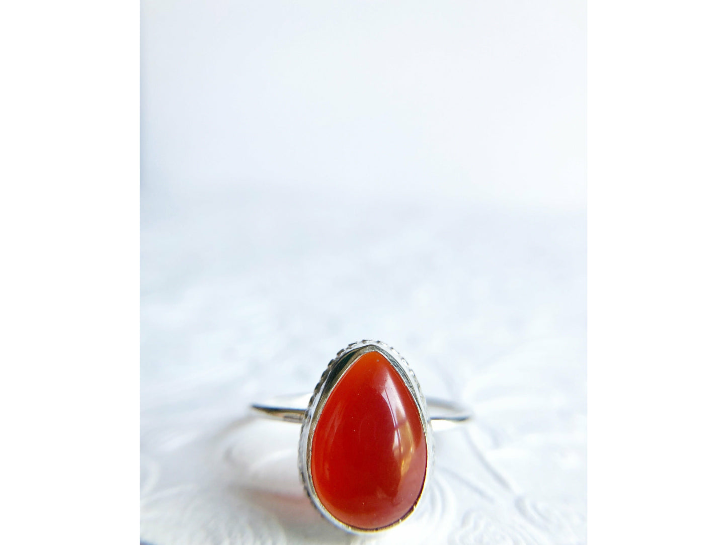 Pear shaped red ring with open back bezel, bezel mounts to the left and right side of the stone.