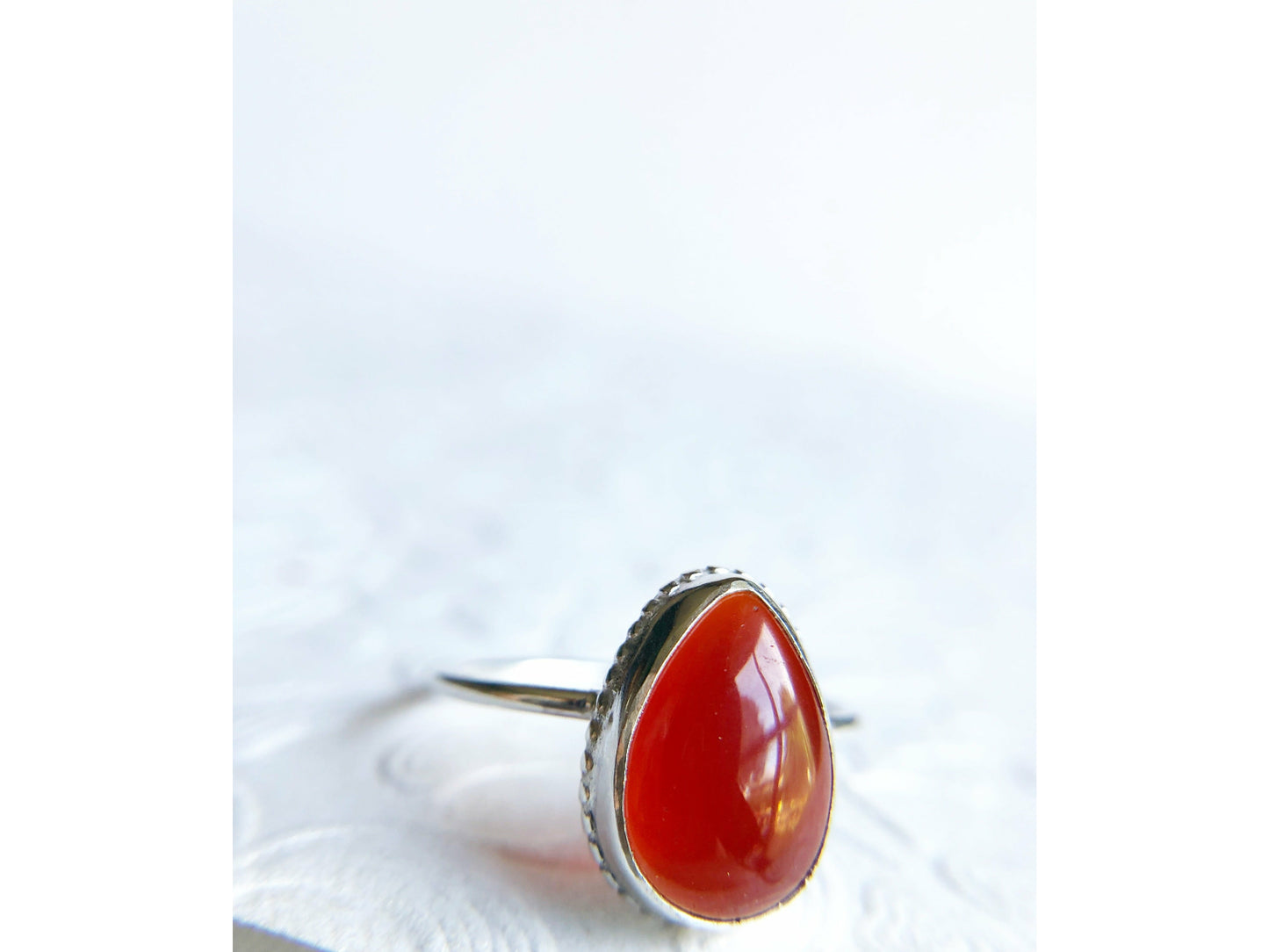 Pear shaped red ring with open back bezel, bezel mounts to the left and right side of the stone.