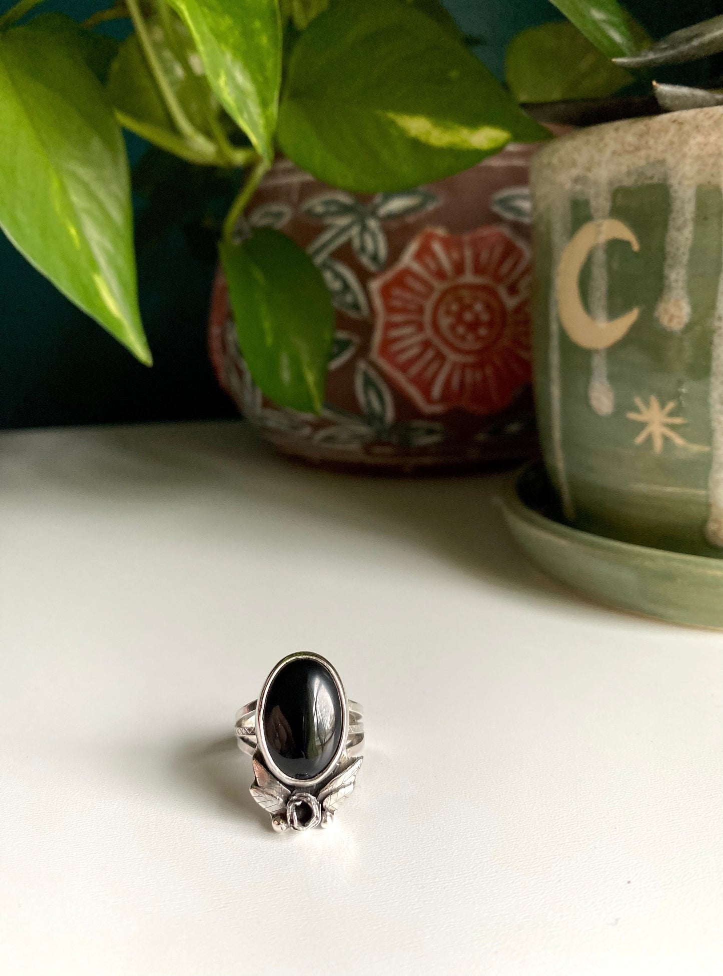 Onyx rose statement ring, Large onyx stone with rose below surrounded by 2 petals on each side, four total. hand carved leaves with two pieces of granulation at bottom. Ring is a triple strand shank two smooth square bands and one square middle band with tiny detail work looking like lattice.