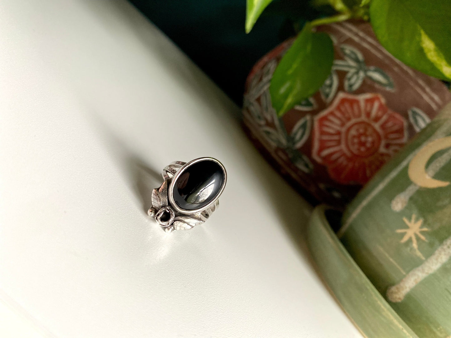 Onyx rose statement ring, Large onyx stone with rose below surrounded by 2 petals on each side, four total. hand carved leaves with two pieces of granulation at bottom. Ring is a triple strand shank two smooth square bands and one square middle band with tiny detail work looking like lattice.