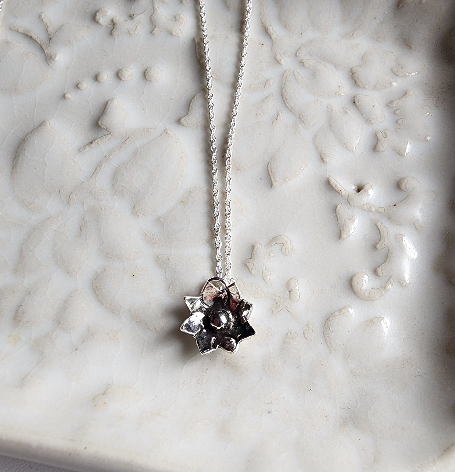Tiny flower pendant hanging from a dainty silver chain