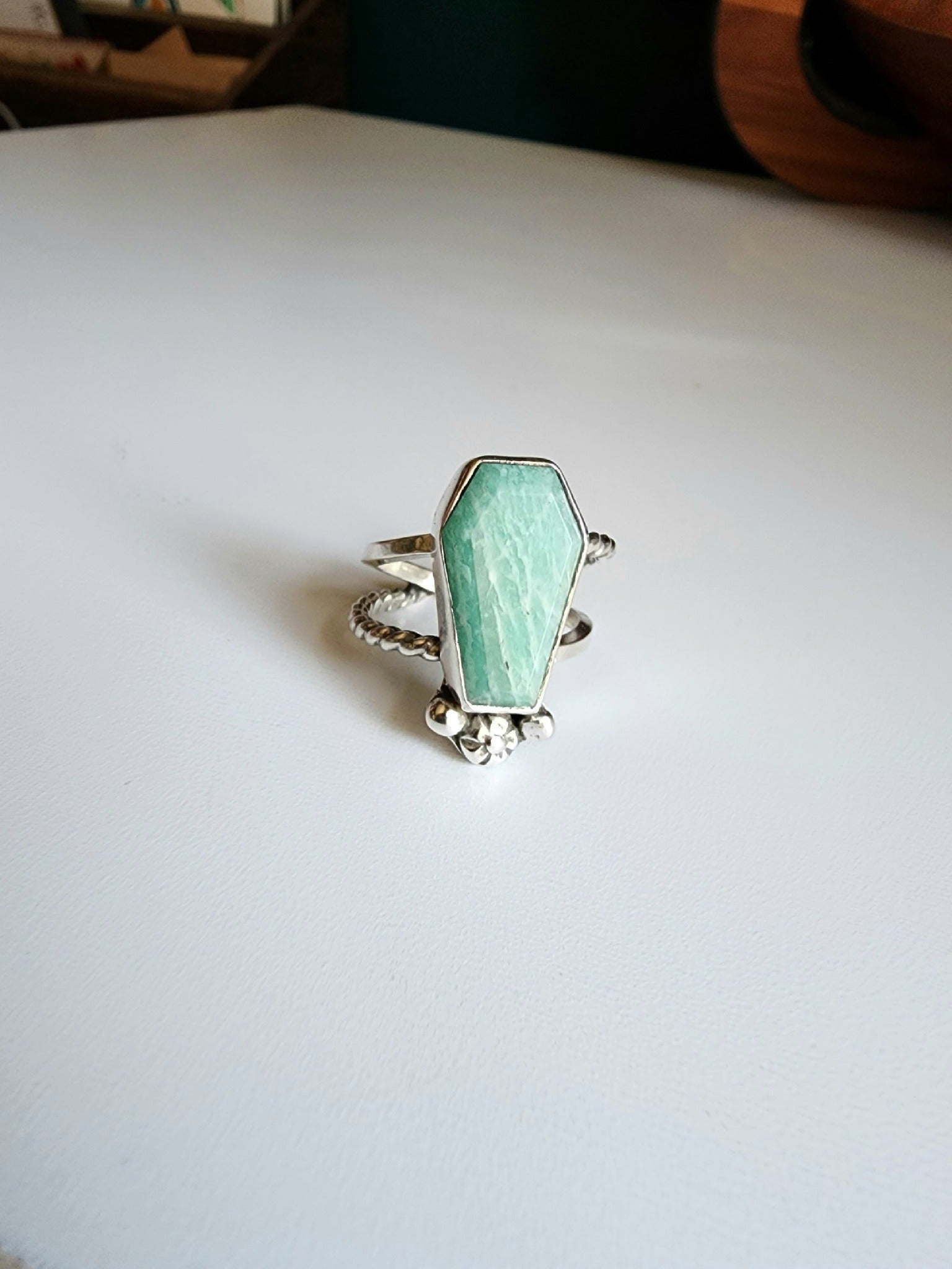 Amazonite coffin stone ring size 7 1/4 split shank with patterned twisted silver on top right and bottom left, square profile on top left and bottom right flower and small granulations on the left and right of small flower at bottom of stone. 