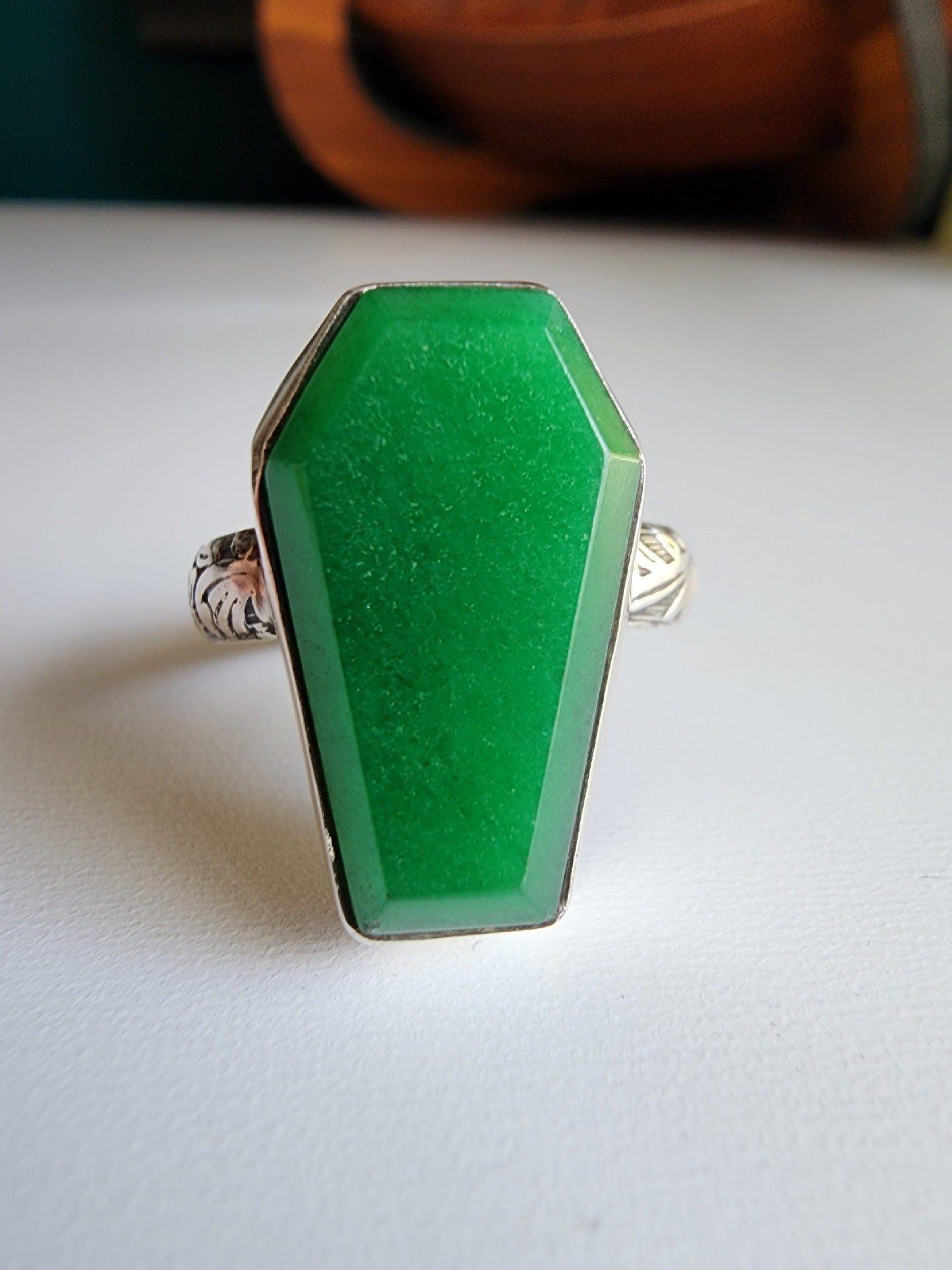 Jade coffin stone shaped stone with simple bezel surround, single band with flowers and vine details that stand out. 