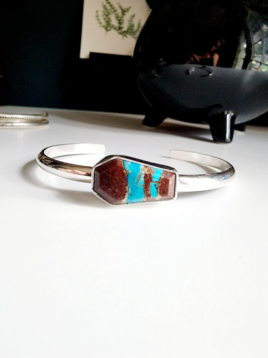 a coffin shaped stone that is blue and red (lave copper turquoise) mounted on a simple sterling silver cuff