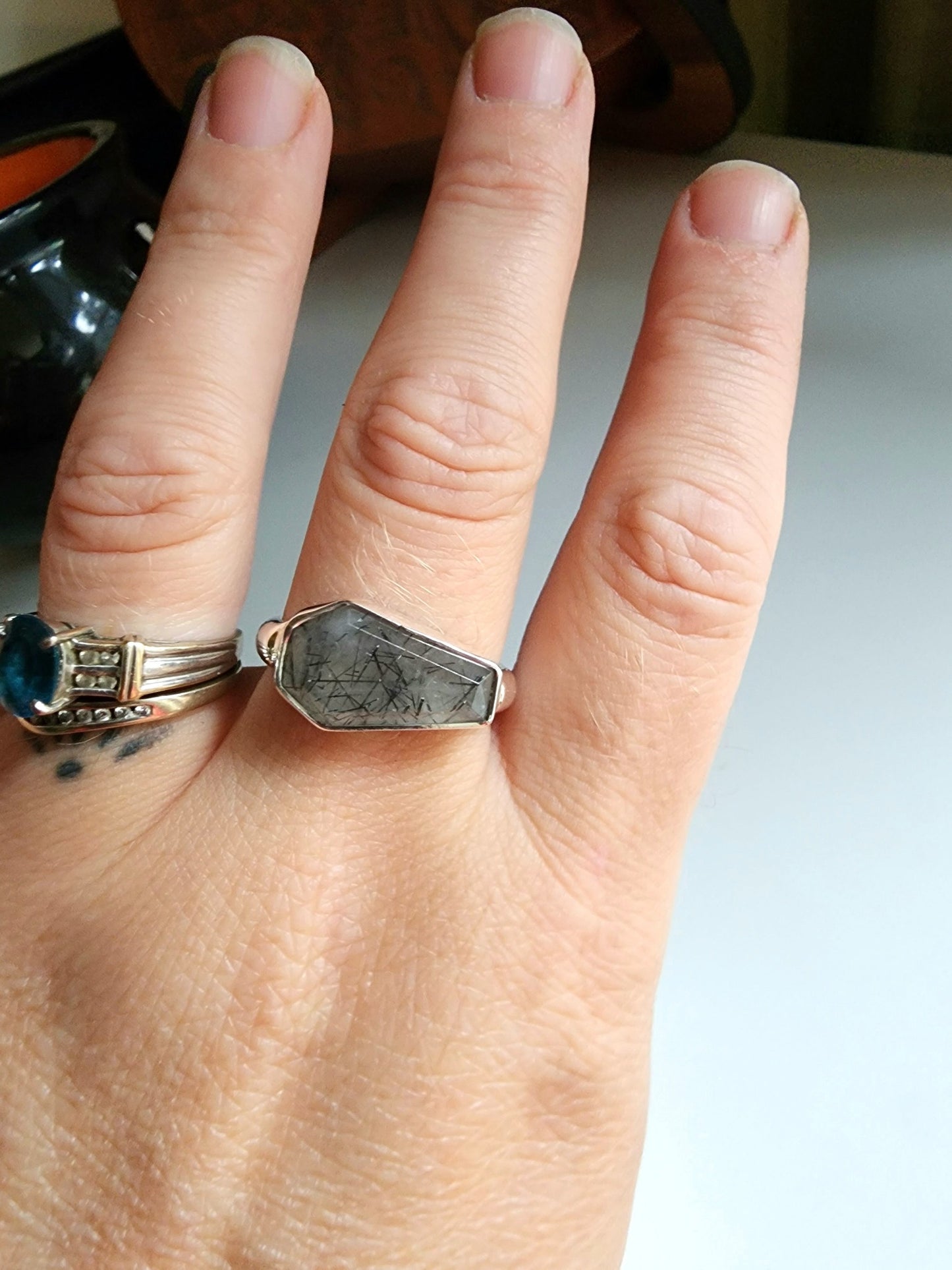 white stone with black flecks with metallic coffin stone shaped ring with thick band that meets the bezel on the left and right 
