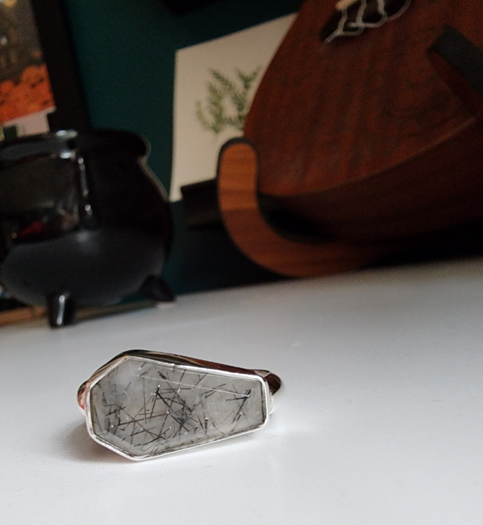 white stone with black flecks with metallic coffin stone shaped ring with thick band that meets the bezel on the left and right 