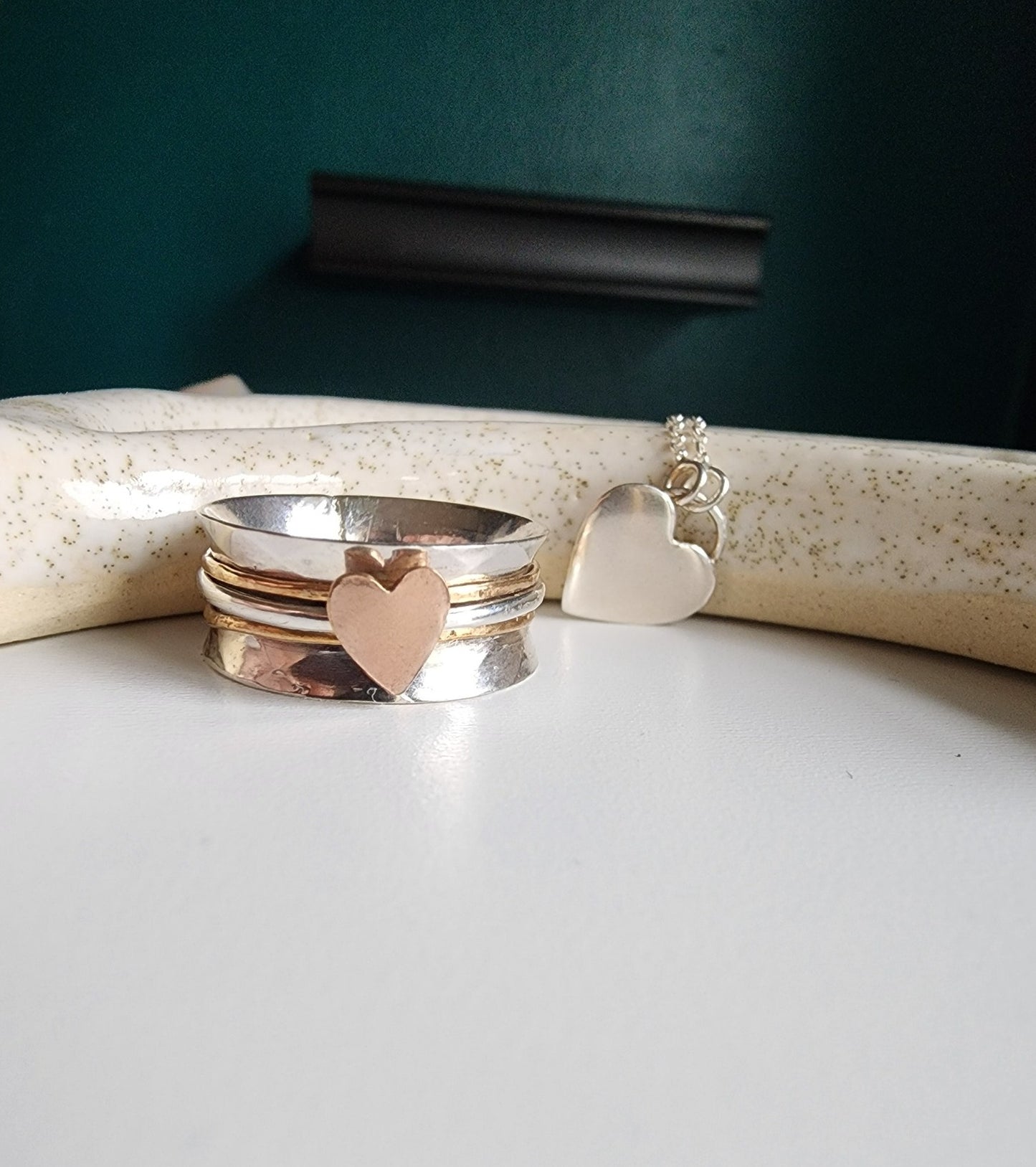 Silver textured wide band ring with three bands top band gold, middle band silver with a rose gold heart, bottom band is gold. Three bands mounted on a wide ring that spin freely, perfect for spinning of rings