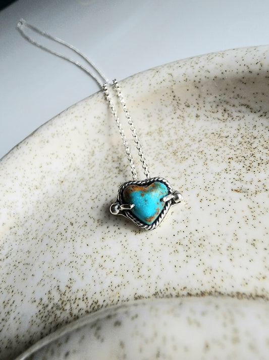 Kingman turquoise heart necklace mounted on a 18 inch sterling silver chain. Heart measures 8mm, surrounded by twist wire and small pieces of ornamental silver on the left and right. Two prong set as well as pressure mounted for security.