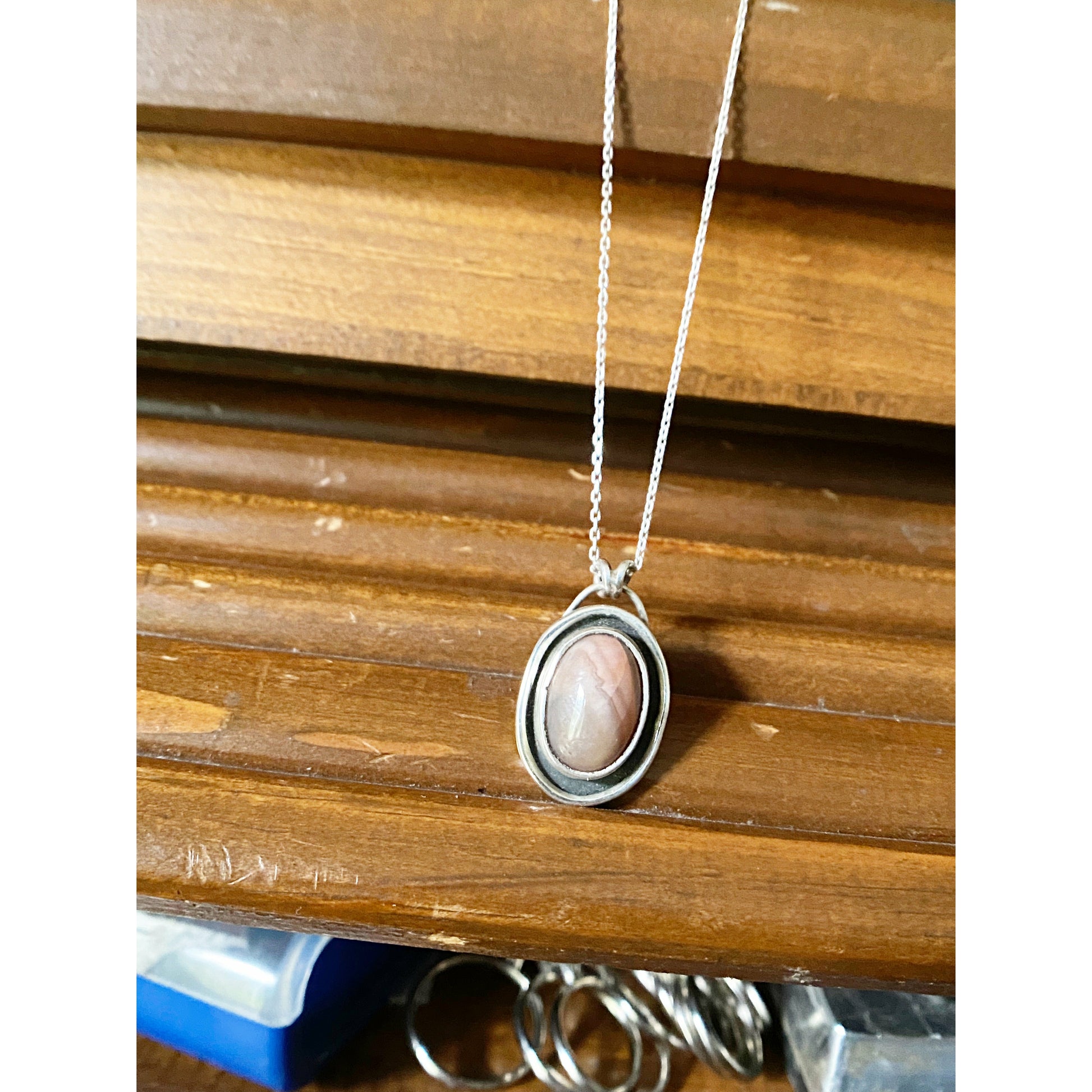Oval pink stone with silver surround encircling stone, mounted on a 18 ich sterling silver necklace this is a choker style chain.