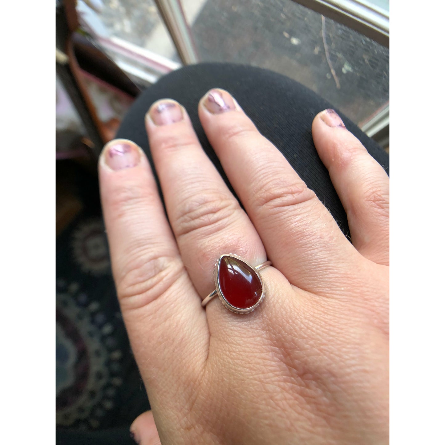 Pear shaped red ring with open back bezel, bezel mounts to the left and right side of the stone.