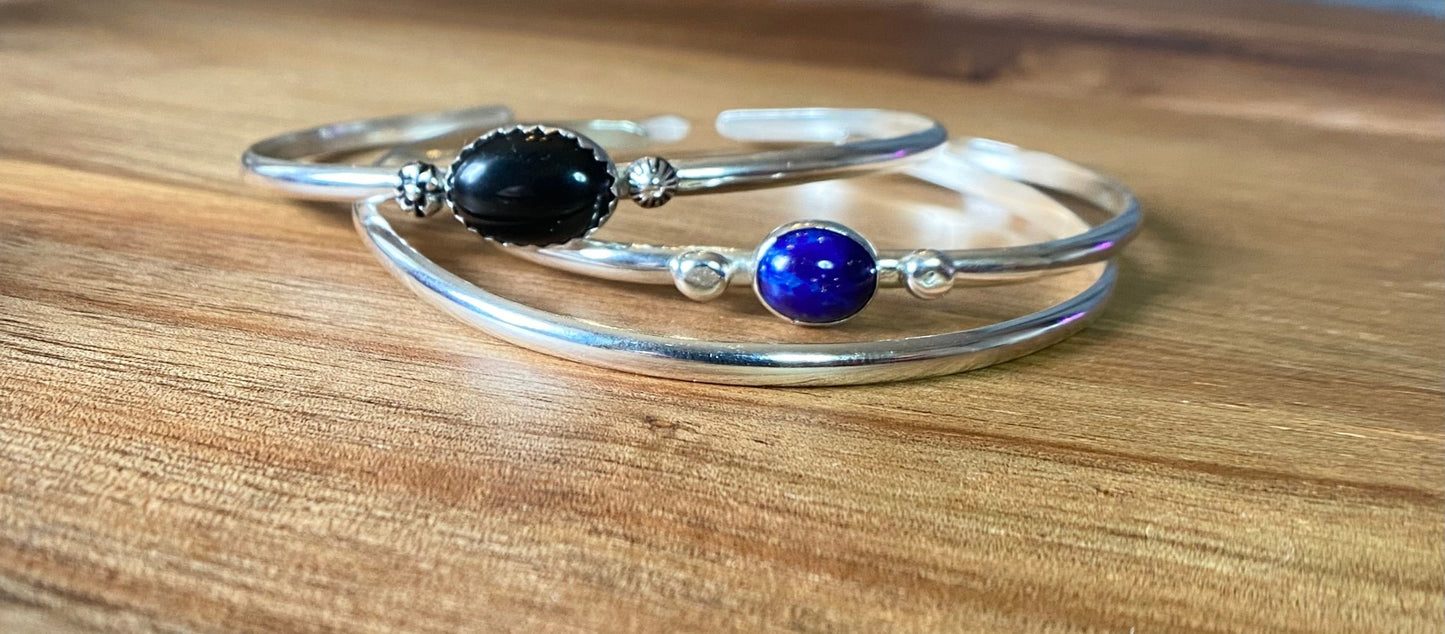 Stacakble cuffs with onyx, lapis or just a plain bracelet. Ornate pieces of silver dot the pieces as well as a oval stone.