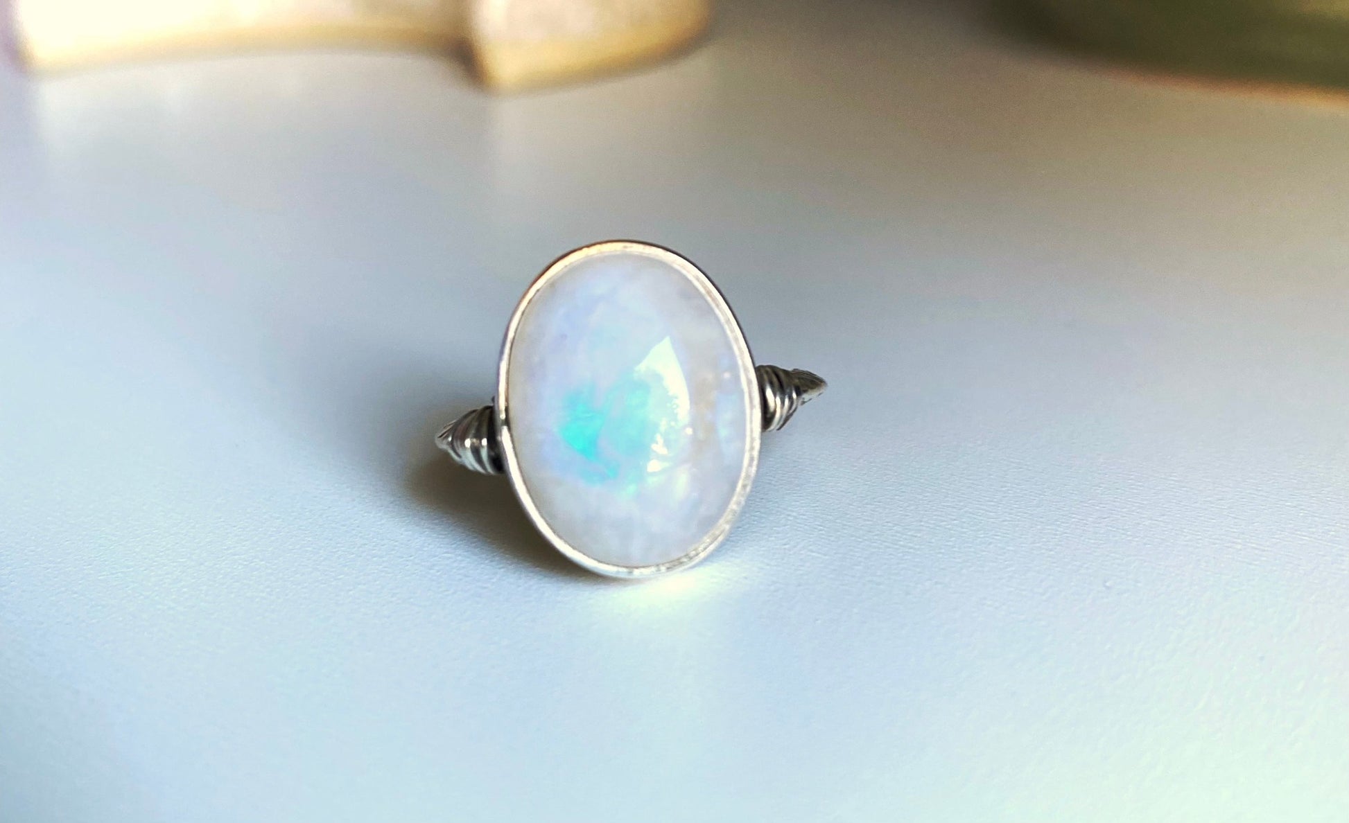 Large moonstone ring with scrollwork single band, left and right of the stone are small sterling silver wire wrapped accents. The moonstone itself has a gorgeous blue flash when the stone is met with direct sunlight. Surrounded by a simple bezel wall to protect the stone.