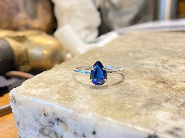 4 Prong set blue faceted teardrop stone, mounted on a square profile ring band