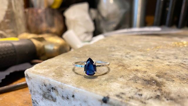4 Prong set blue faceted teardrop stone, mounted on a square profile ring band