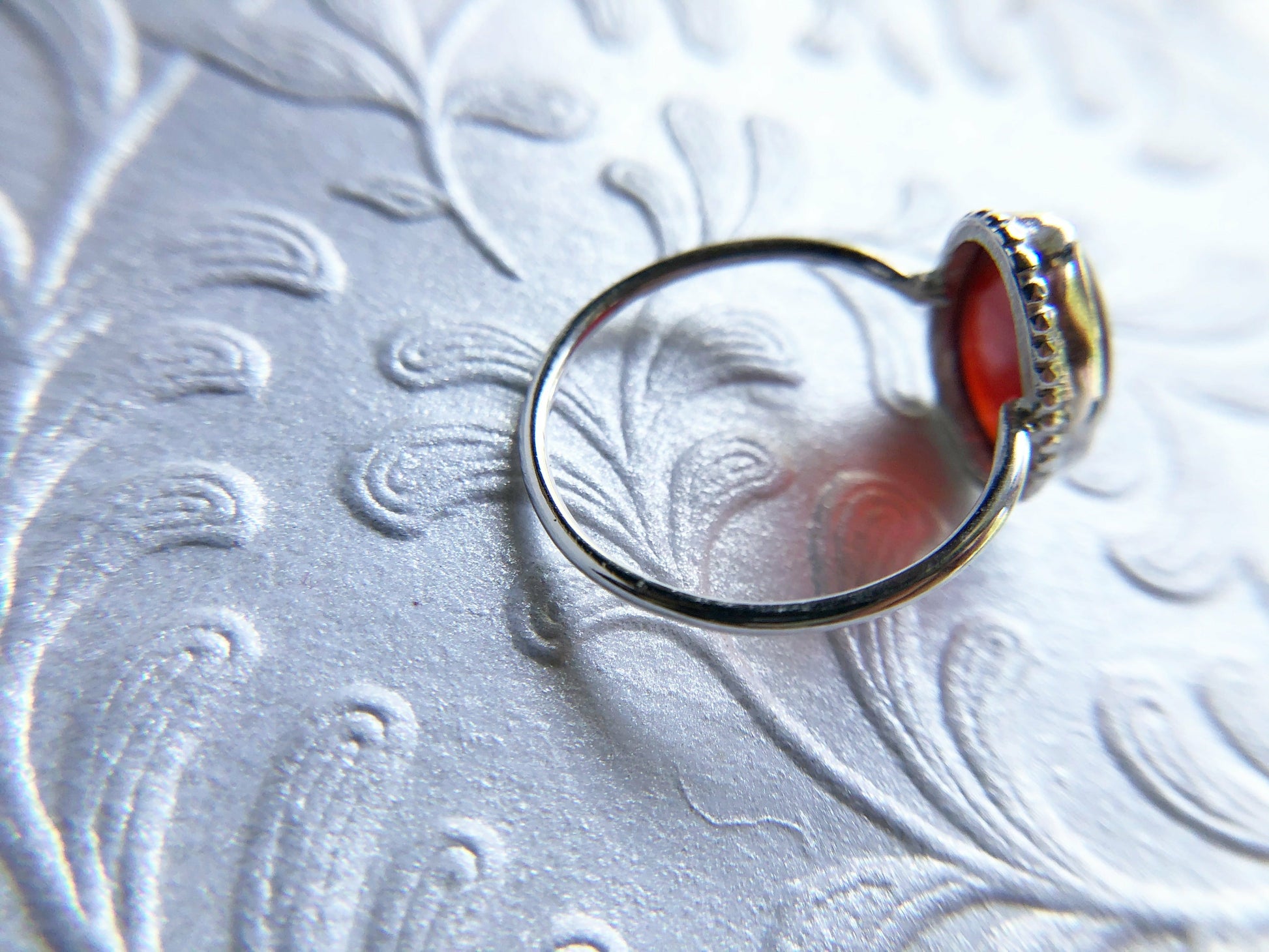 Pear shaped red ring with open back bezel, bezel mounts to the left and right side of the stone.
