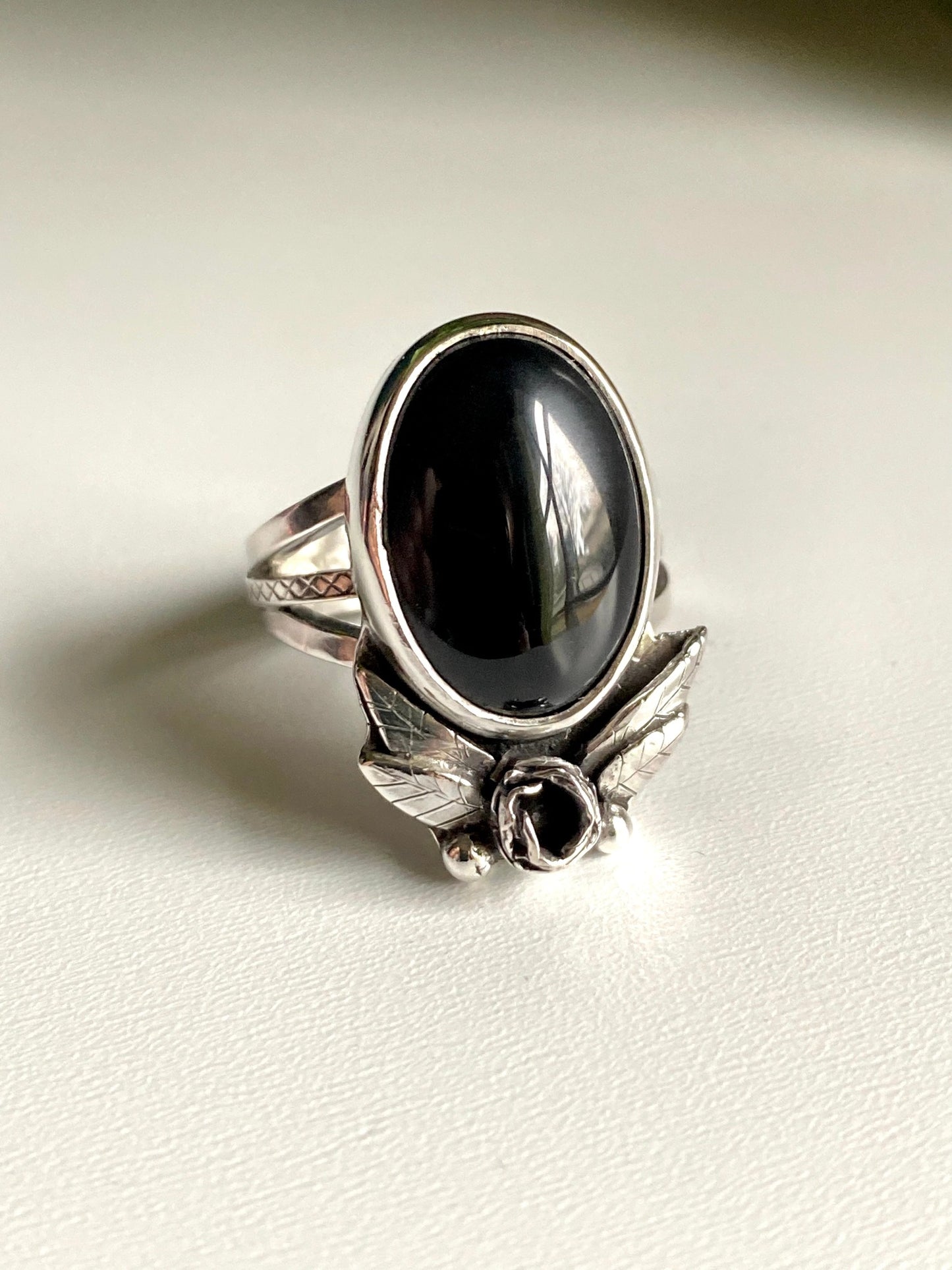 Onyx rose statement ring, Large onyx stone with rose below surrounded by 2 petals on each side, four total. hand carved leaves with two pieces of granulation at bottom. Ring is a triple strand shank two smooth square bands and one square middle band with tiny detail work looking like lattice.